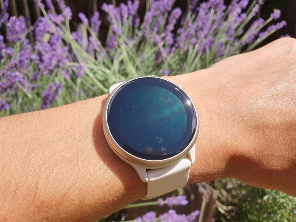 A person wearing a smart watch with lavender flowers in the background.